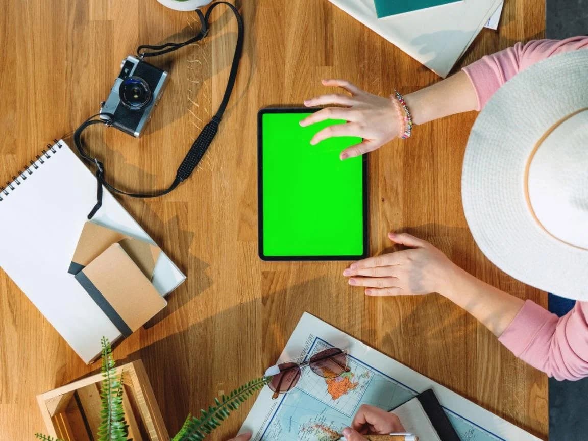 Vista de cima de uma mesa de trabalho com tablet, cadernos, câmera e duas pessoas fazendo anotações